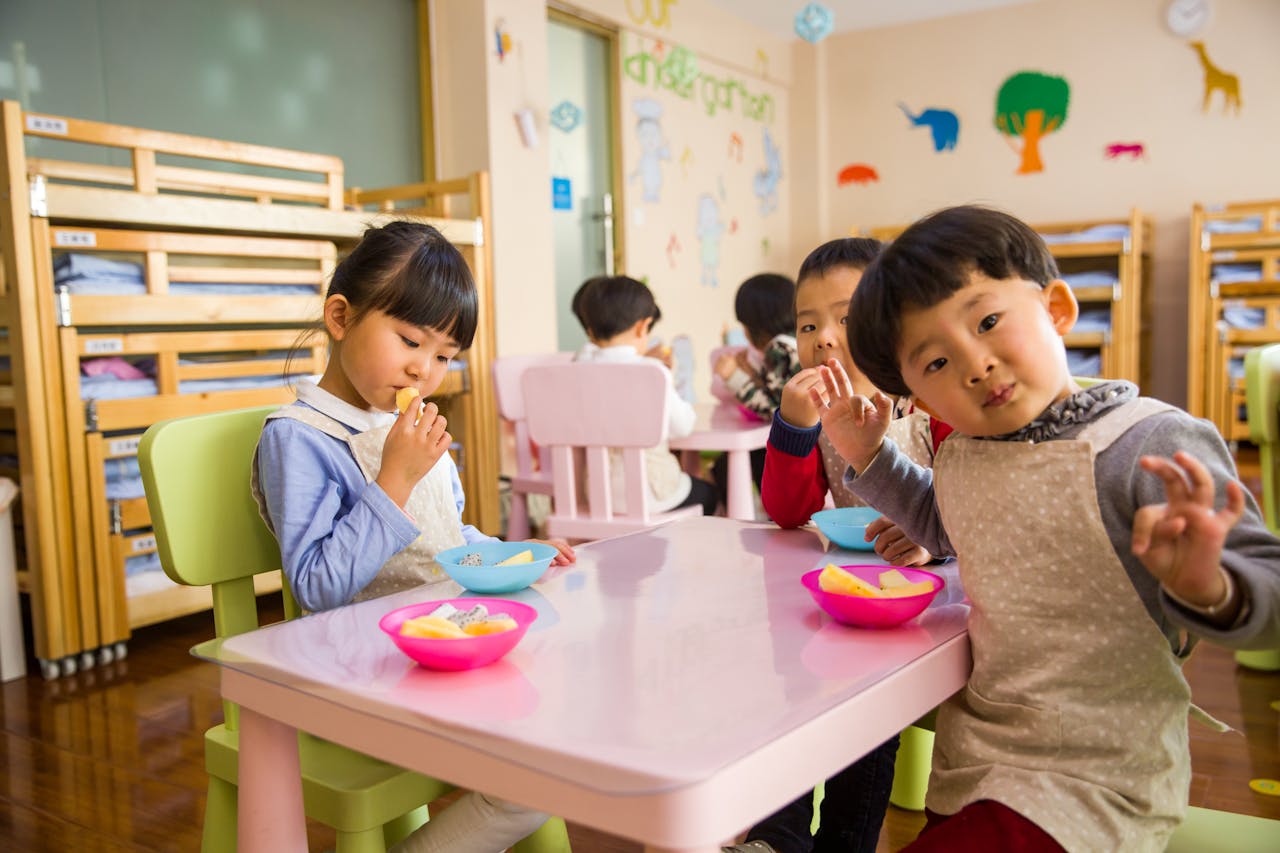 our-story Kids seated around a table in a colorful classroom, eating snacks happily.